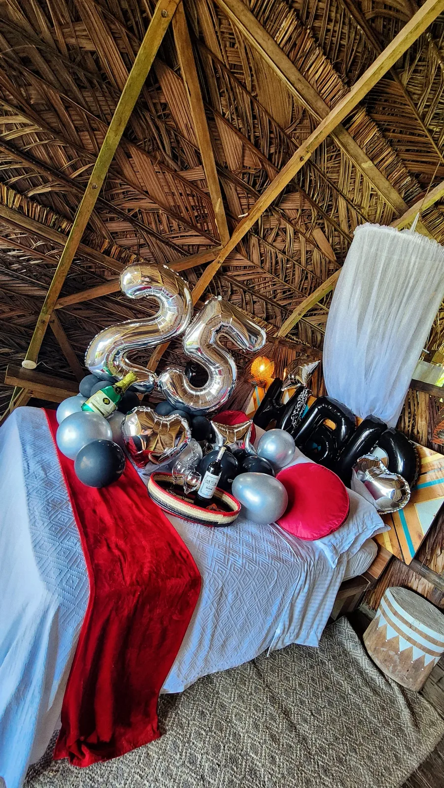 Decoración de aniversario número 25 con globos plateados y detalles rojos sobre la cama.