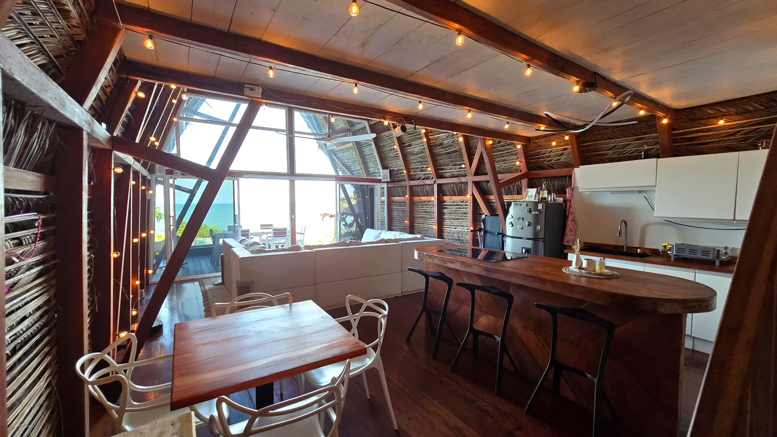 Comedor y cocina abierta con vista hacia la terraza y el mar.