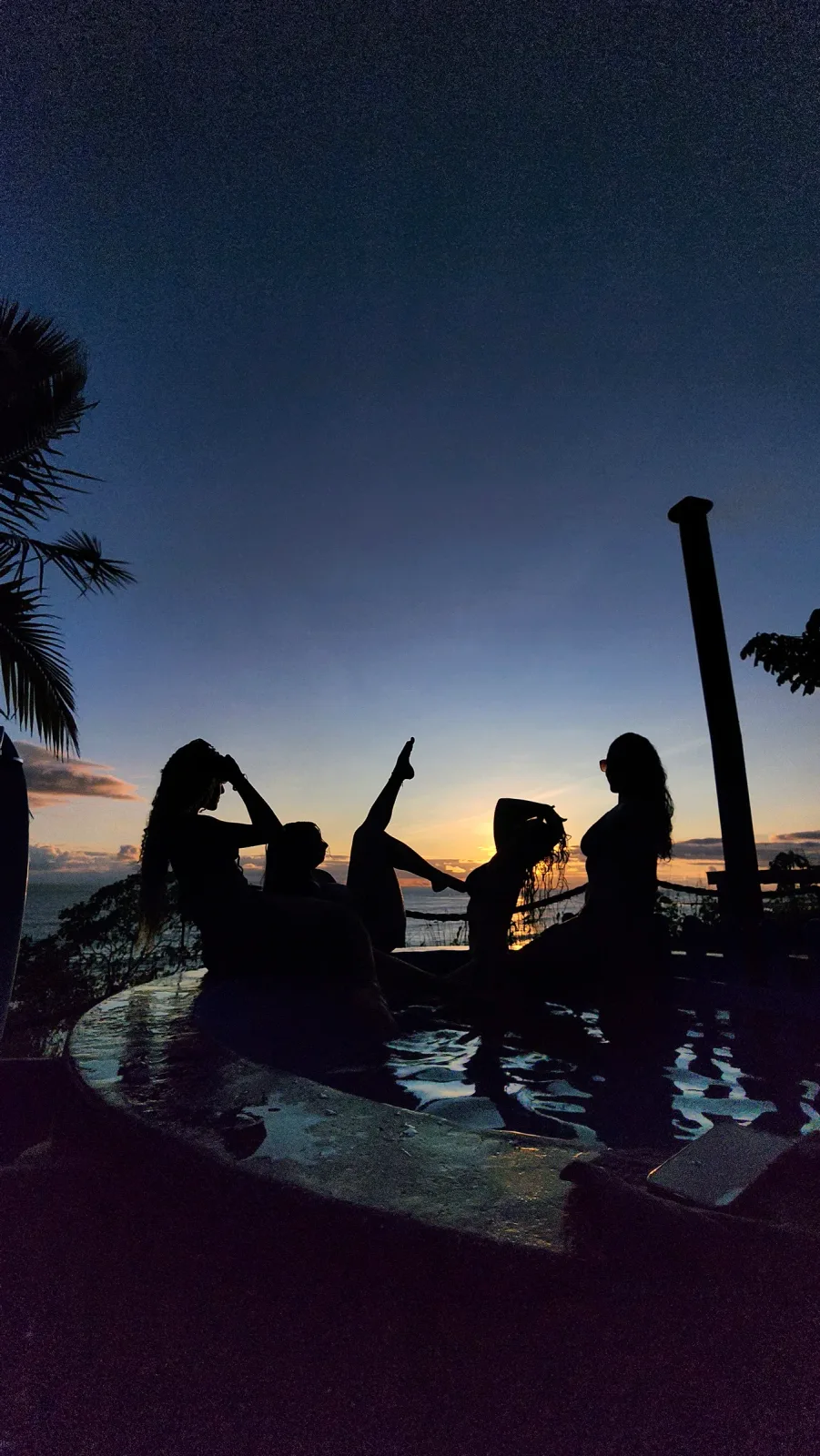 Grupo de amigos en una piscina frente al mar durante el atardecer.