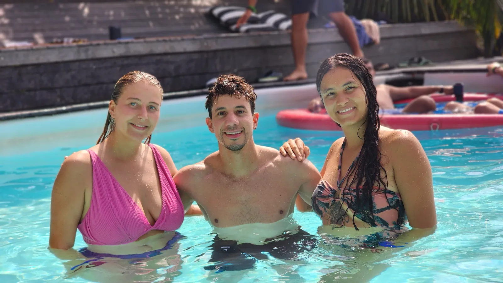 Tres amigos sonriendo dentro de una piscina al aire libre.