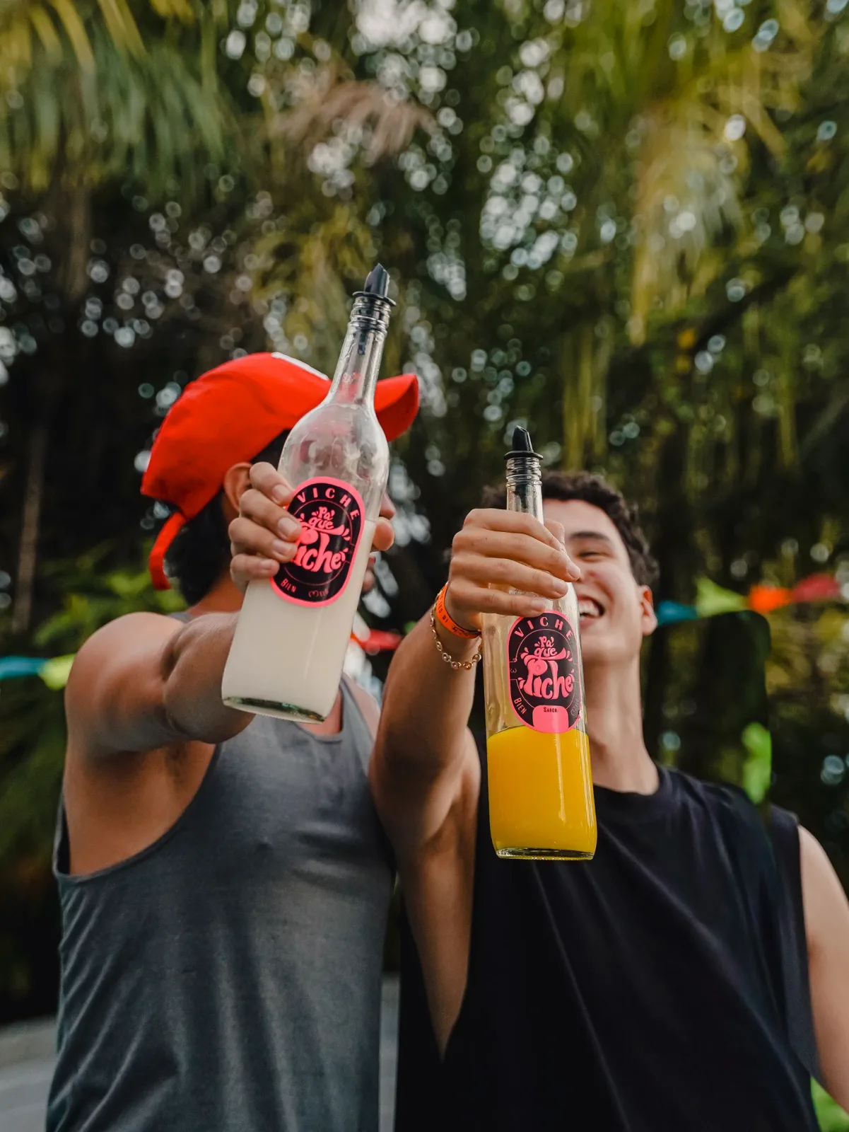 Dos visitantes brindando con botellas de bebidas tropicales.