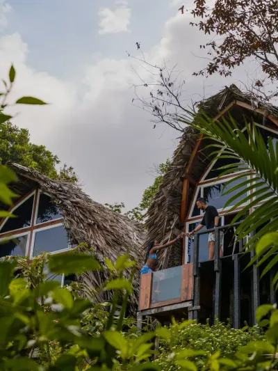 Cabaña triangular elevada con balcón y techo de palma entre la vegetación.