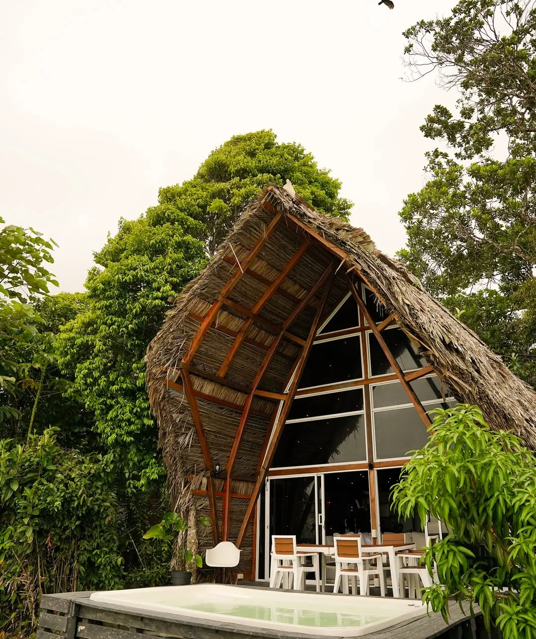 Cabaña triangular de techo de palma con piscina privada y terraza.