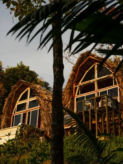 Dos cabañas triangulares de techo de palma iluminadas por el atardecer.