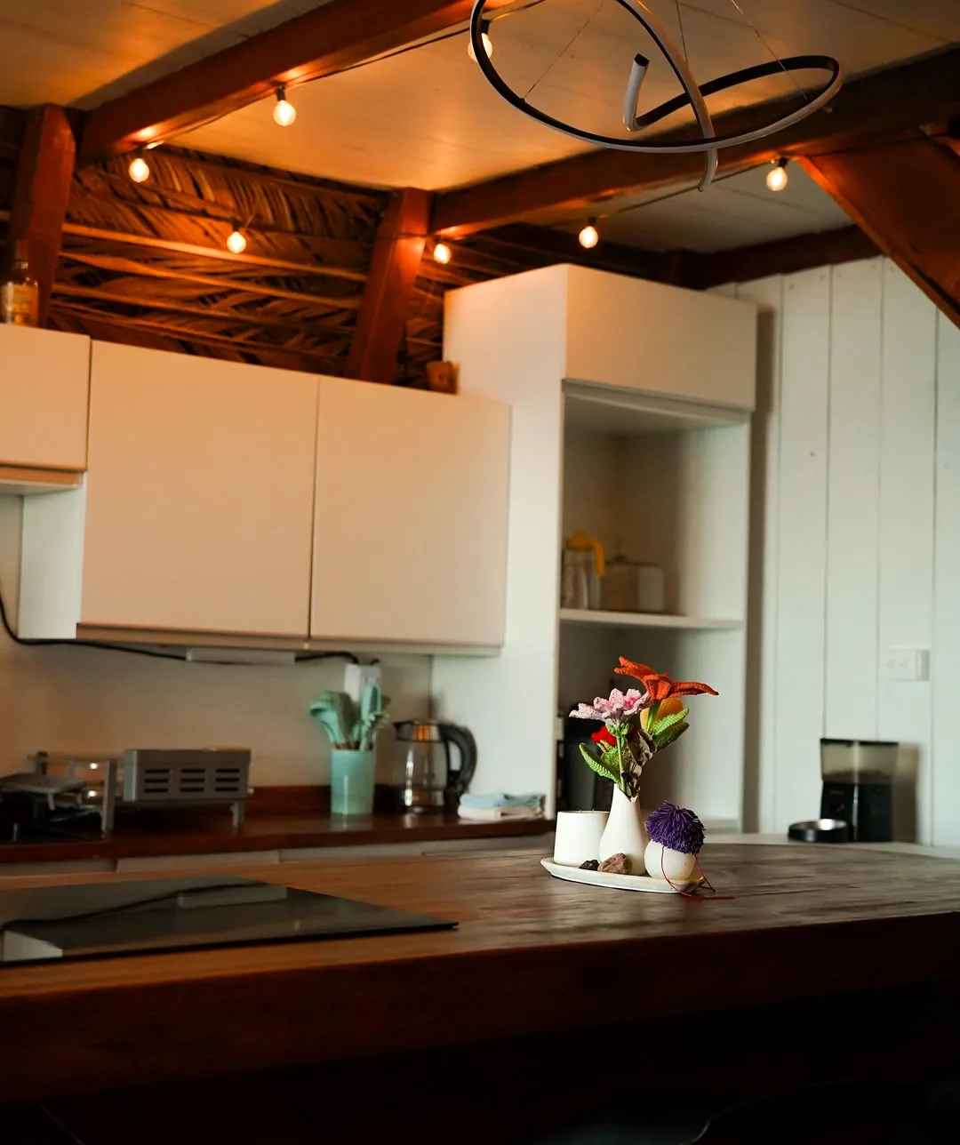 Cocineta con gabinetes de madera, iluminación cálida y flores.