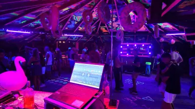 Cabina del DJ en primer plano y público bailando bajo luces neón.