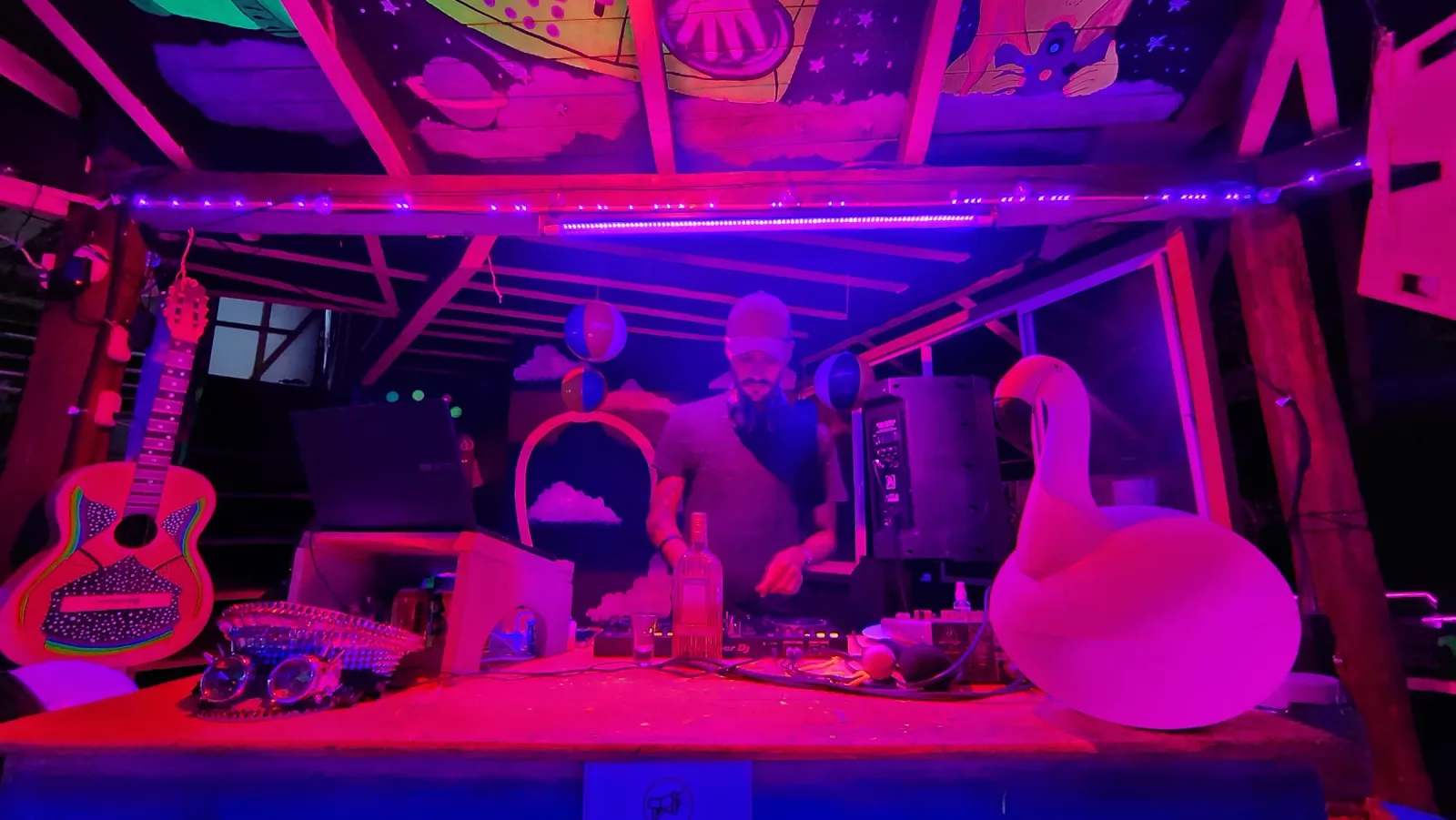 Dos DJs en una cabina iluminada en rosa durante la fiesta.