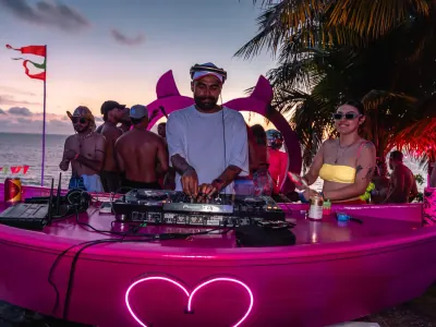Dos DJs en una cabina rosa frente al mar durante un evento al atardecer.