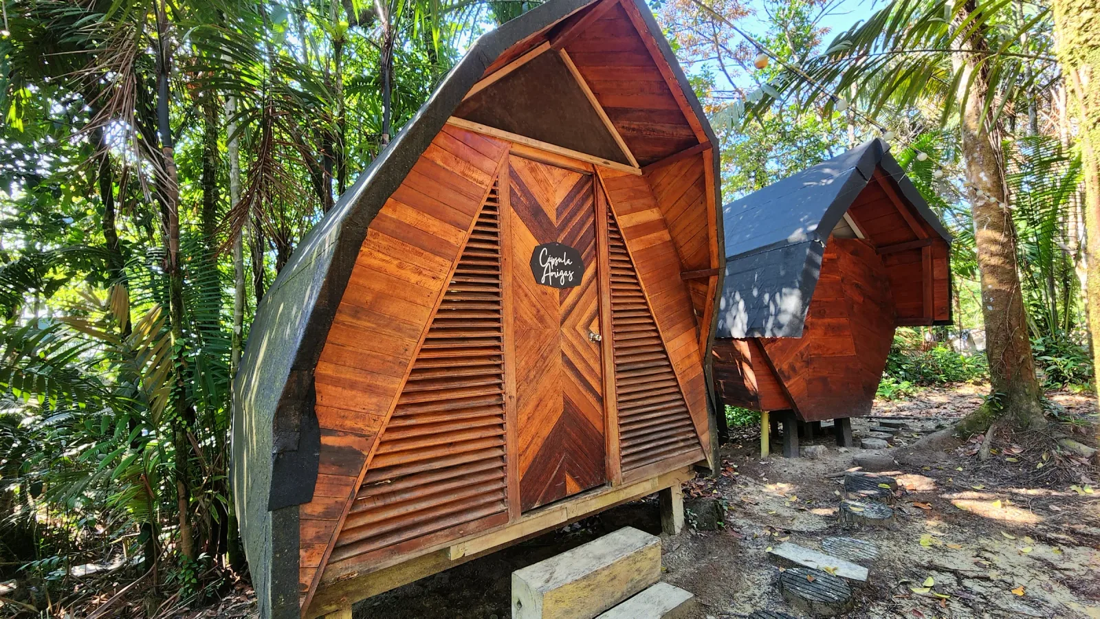 Fachadas triangulares de cabañas de madera rodeadas por bosque tropical.