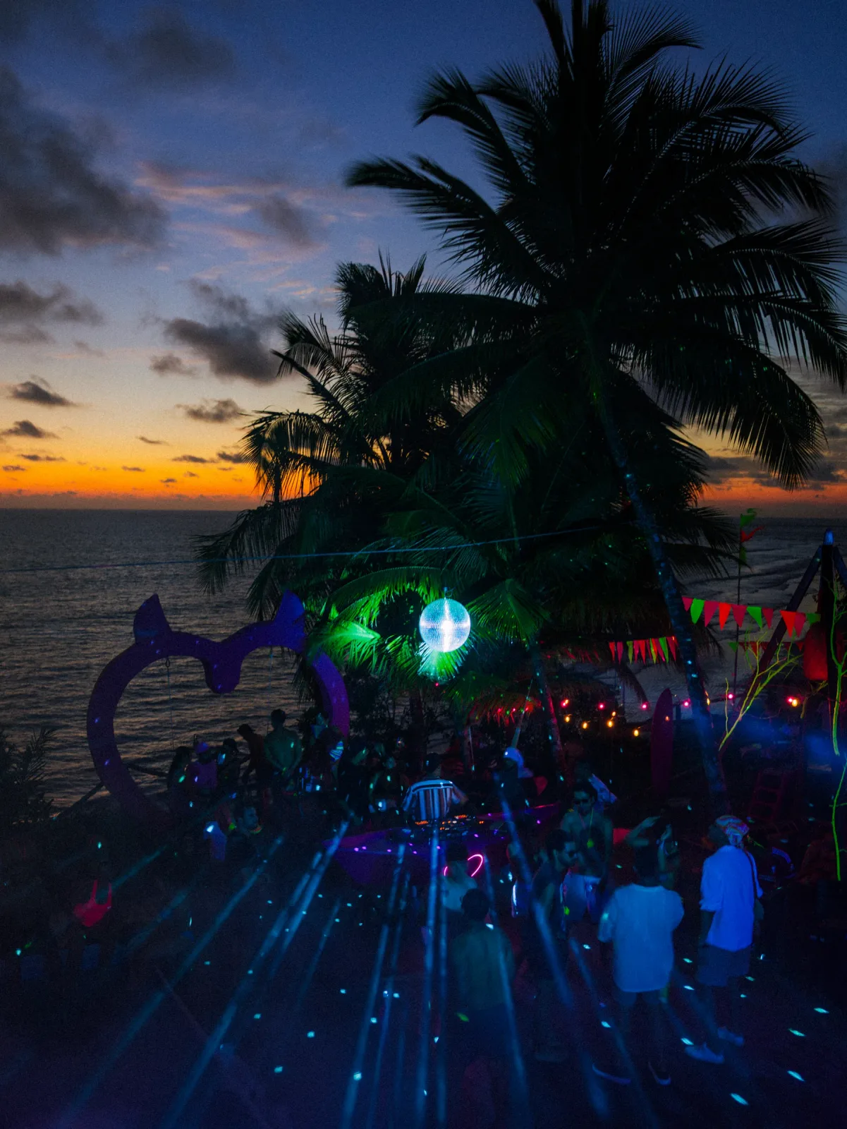 Vista amplia de una fiesta nocturna entre palmeras frente al mar.