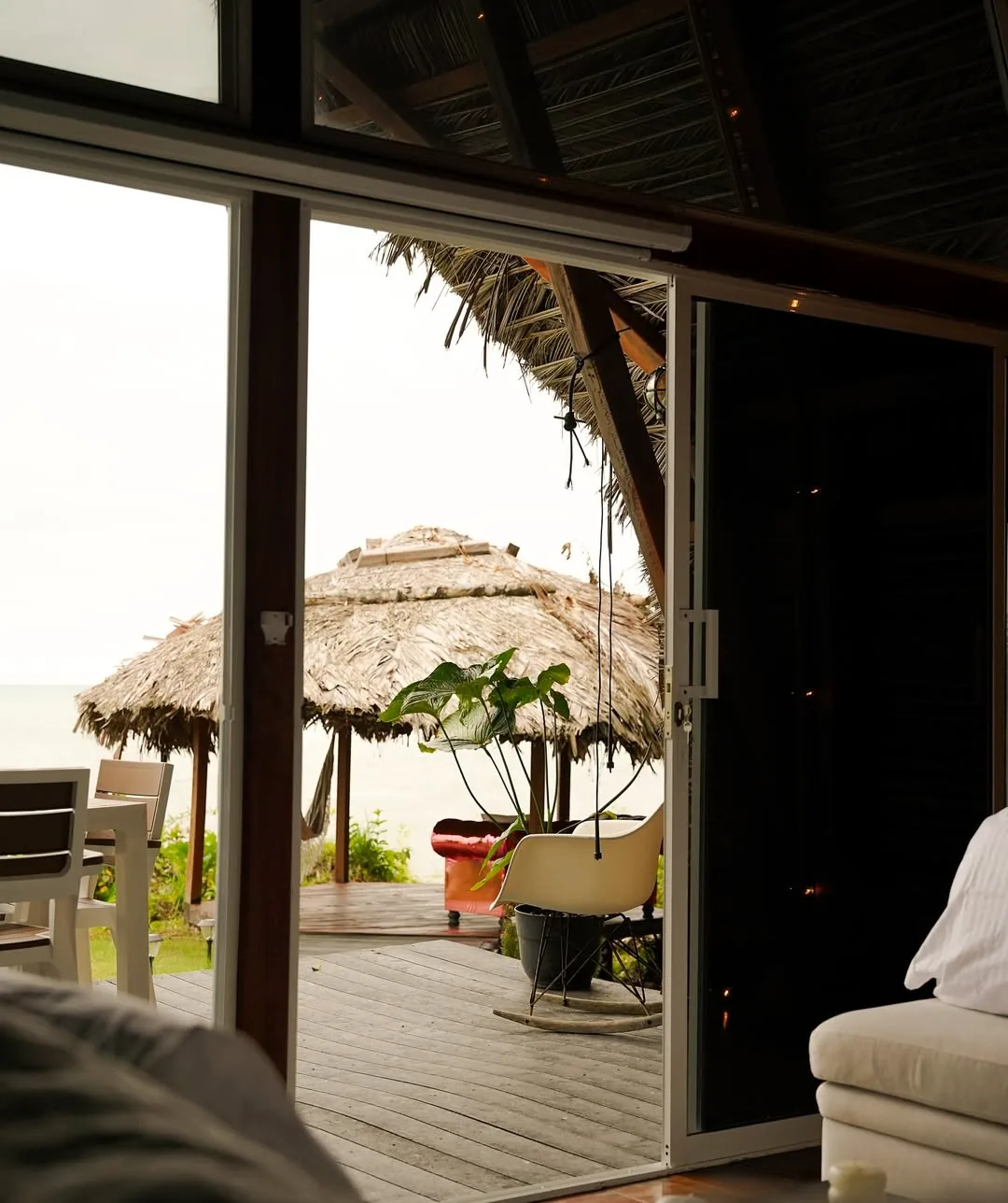 Habitación abierta hacia una terraza tropical con mobiliario blanco.