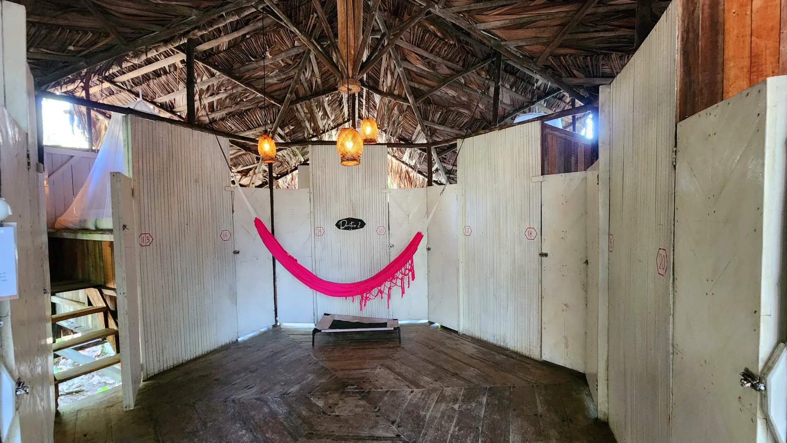 Zona común de los dormitorios cápsula con hamaca rosa y puertas individuales.