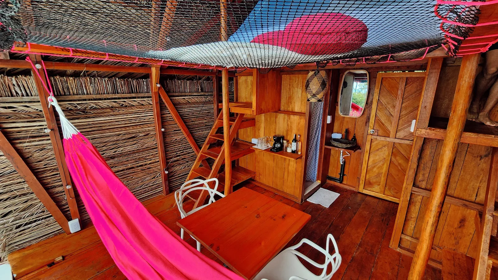 Interior de madera con hamaca rosa, baño privado y zona de almacenamiento.