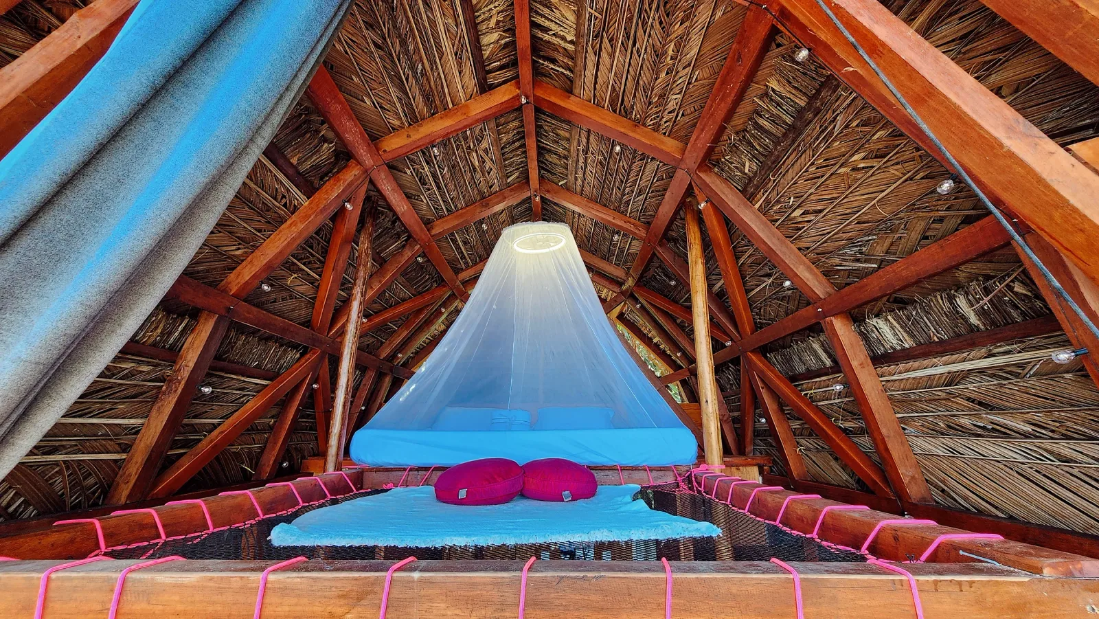 Cama con mosquitero centrada bajo la estructura triangular de madera.