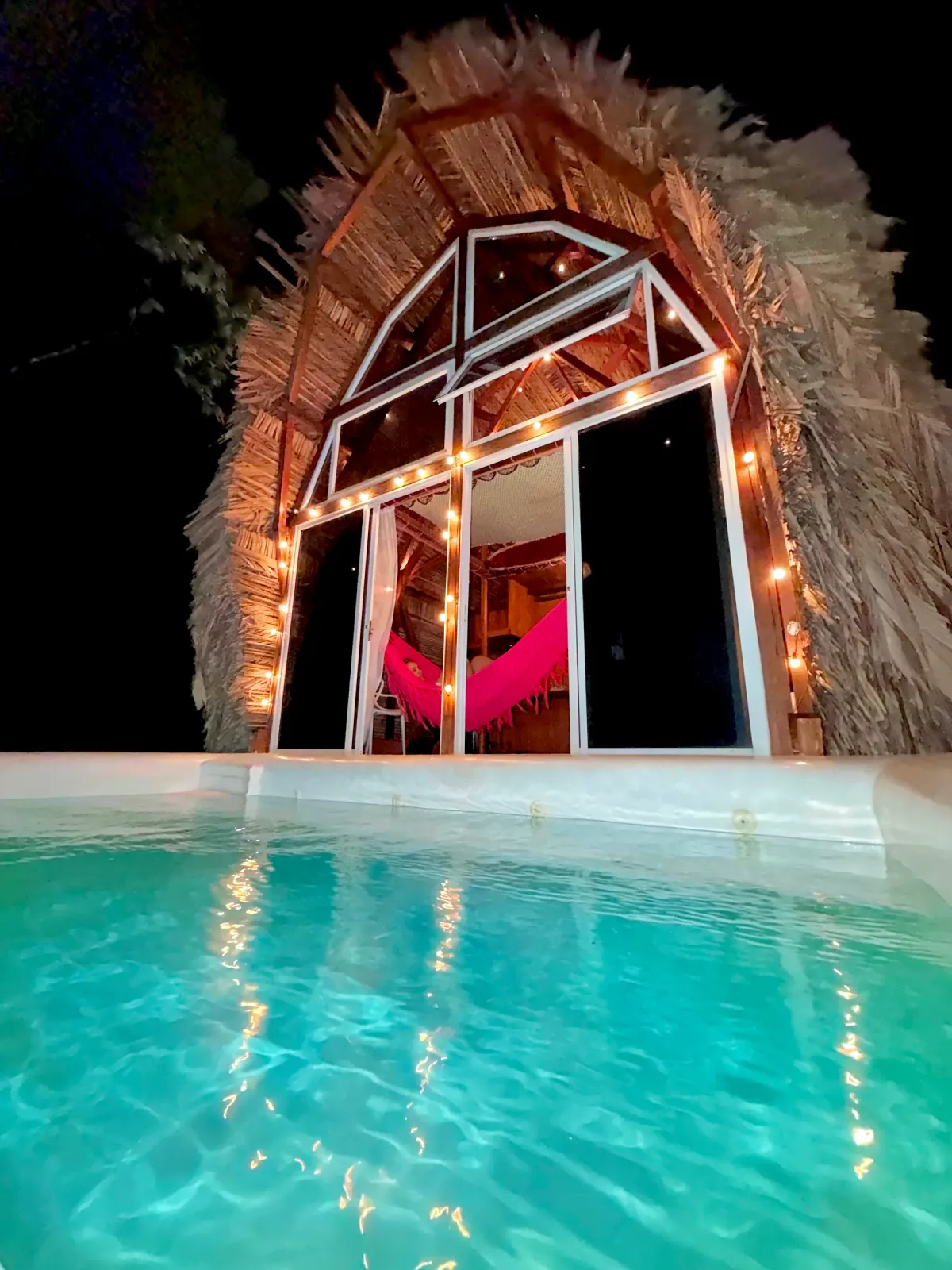 Fachada de Metemelo iluminada de noche junto a la piscina.