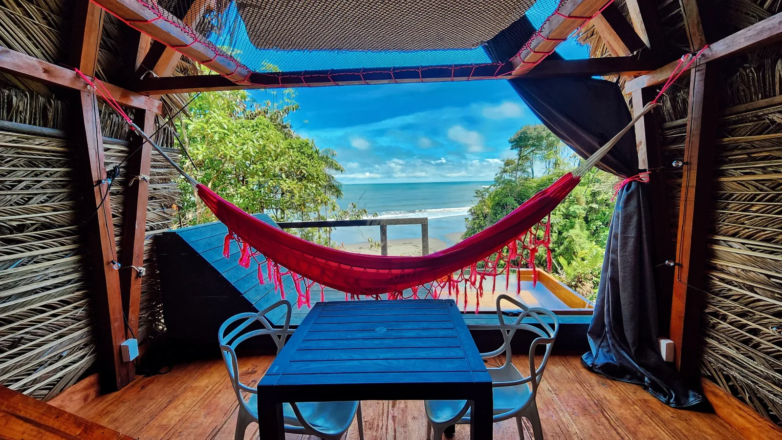 Terraza con hamaca rosa y mesa frente a una vista abierta del océano.