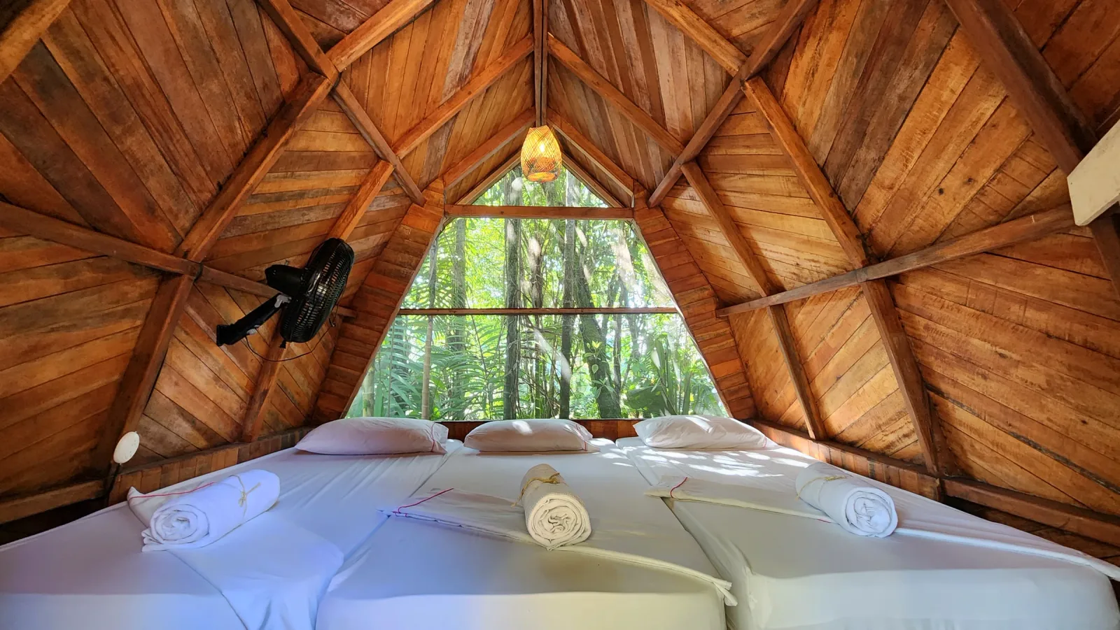 Habitación de cabaña con dos camas, techo triangular de madera y vista verde.