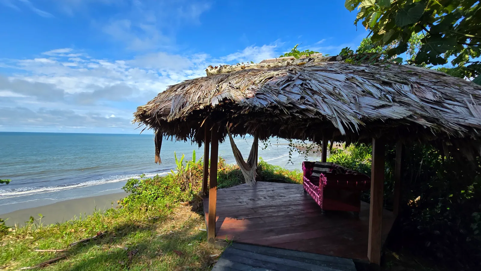Kiosco de descanso con techo de palma y vista al océano.