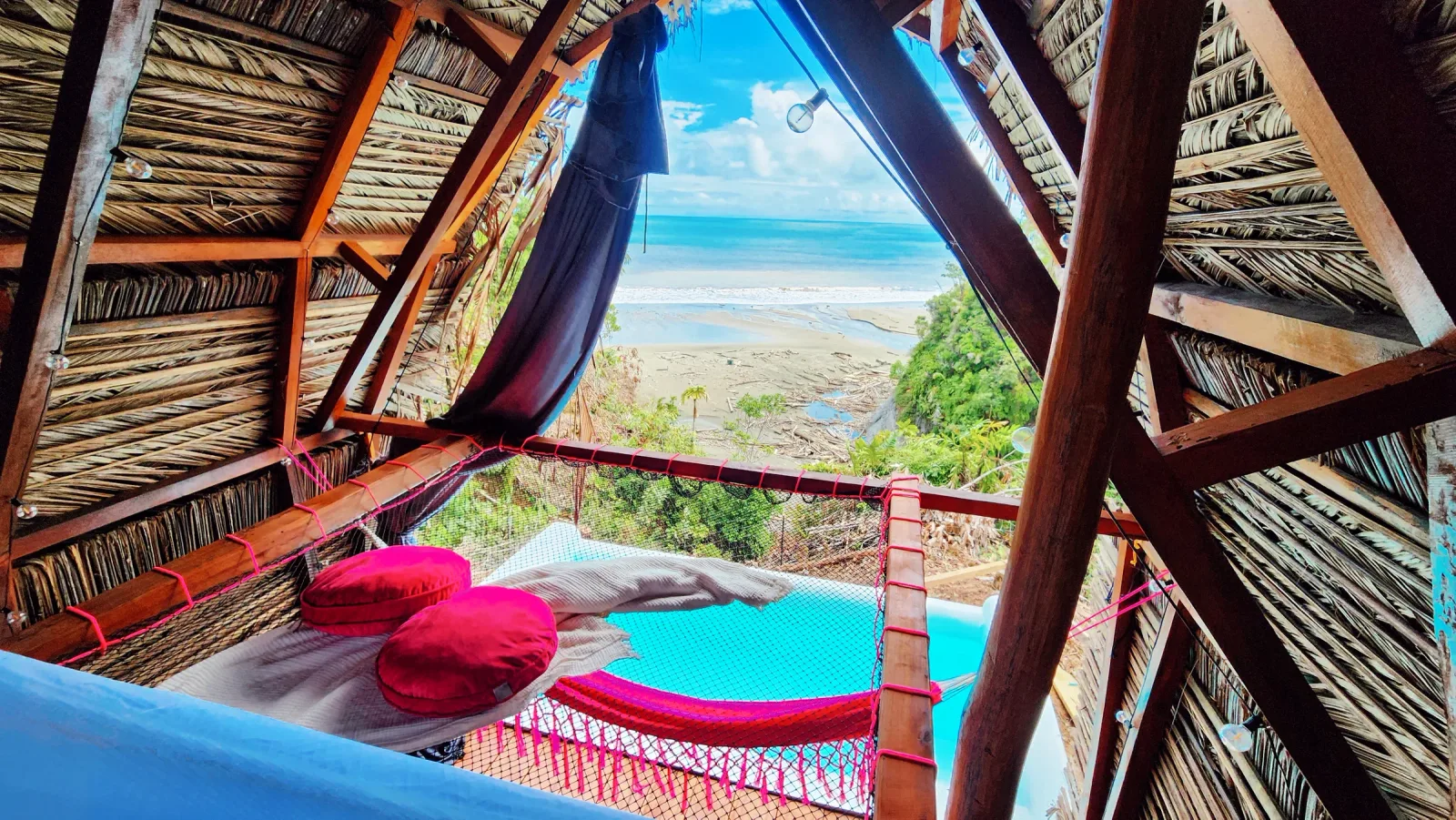 Habitación rústica con cama y vista directa al mar desde una abertura triangular.