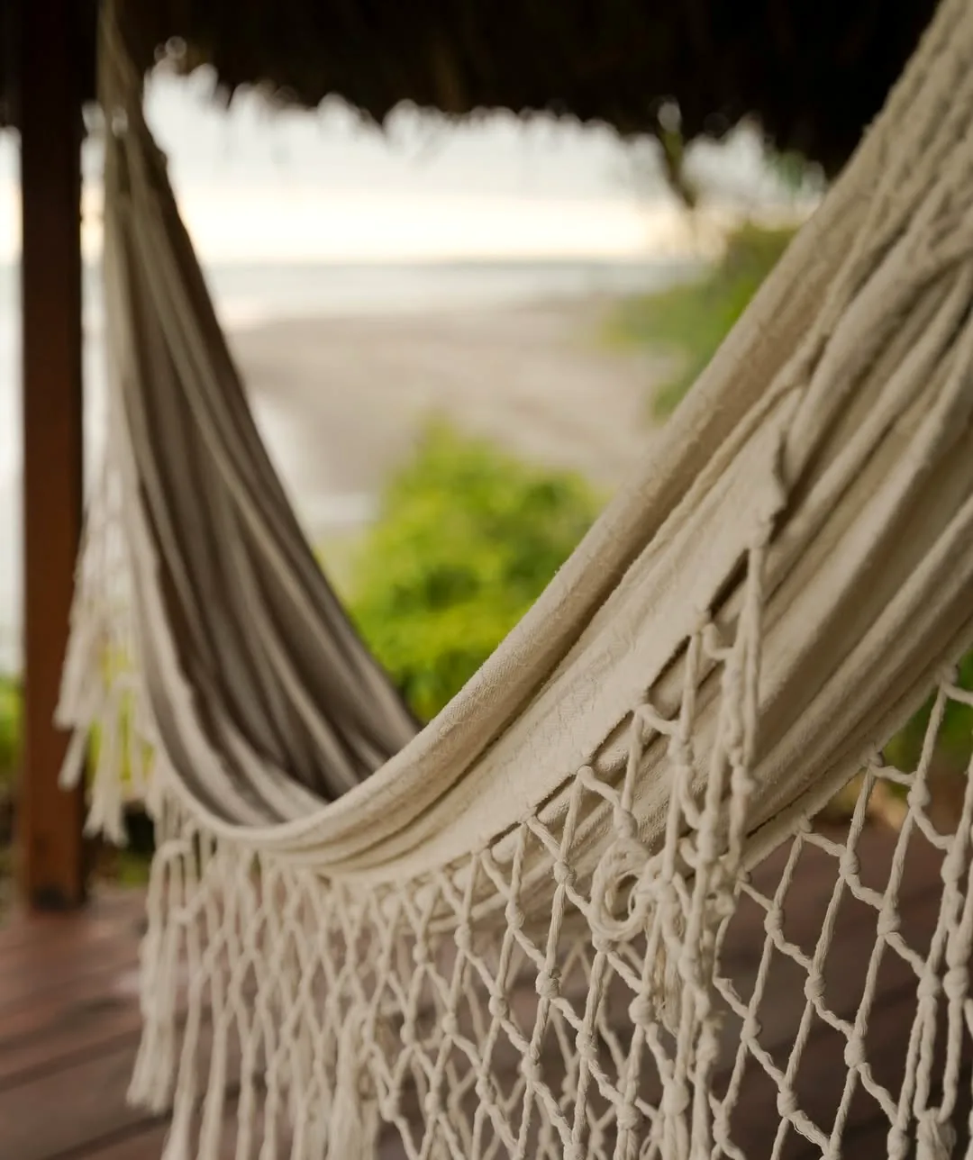Detalle de una hamaca artesanal blanca con la playa desenfocada al fondo.