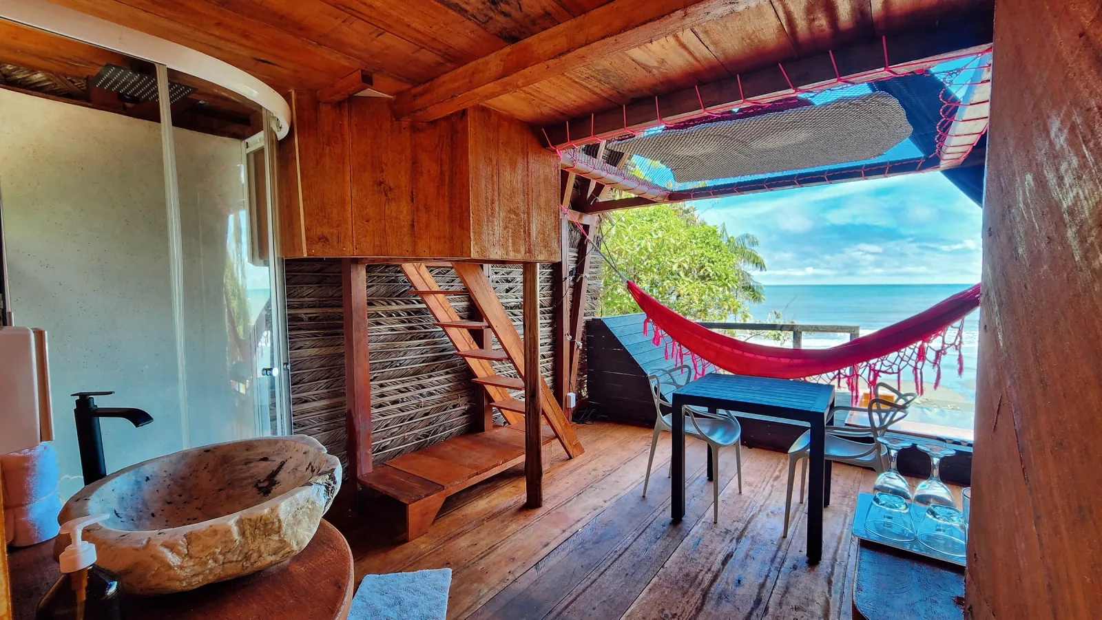 Interior rústico de madera con hamaca roja y vista abierta al océano.