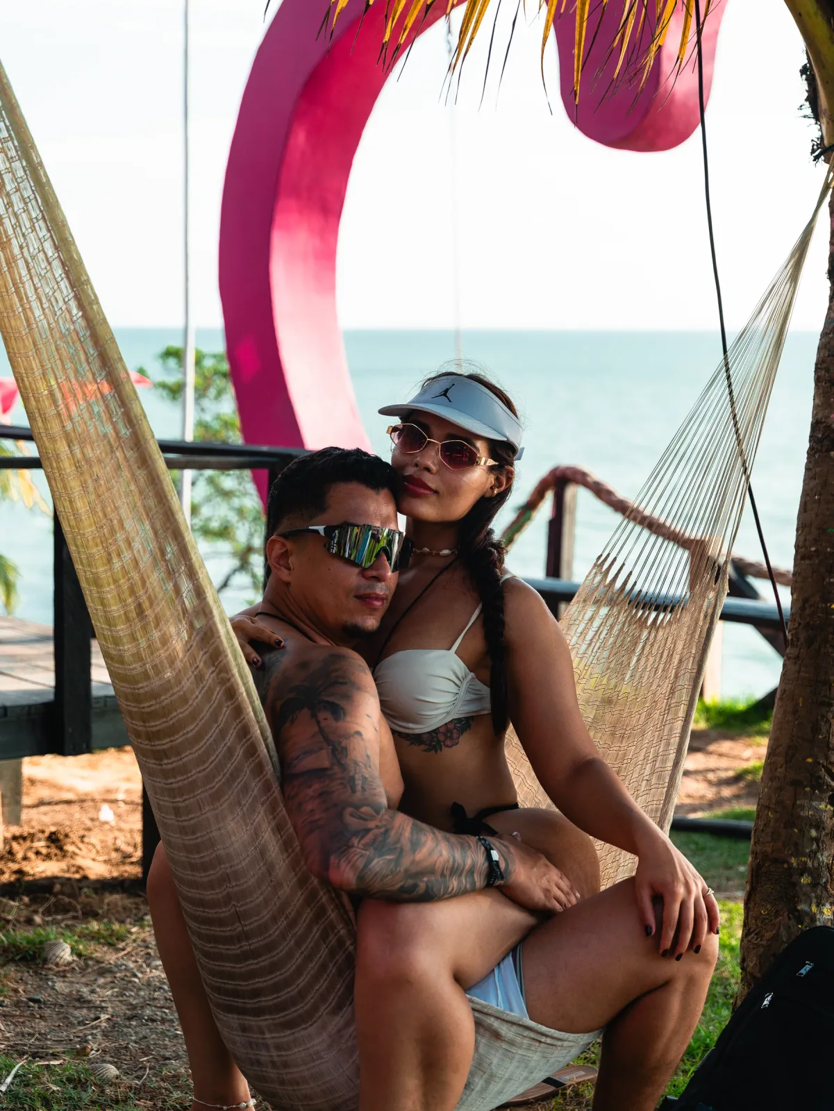 Pareja descansando en una hamaca junto al columpio rosa frente al mar.