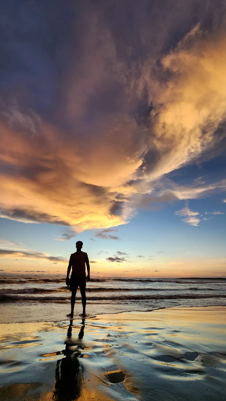 Persona reflejada en la arena mojada de la playa durante el atardecer.