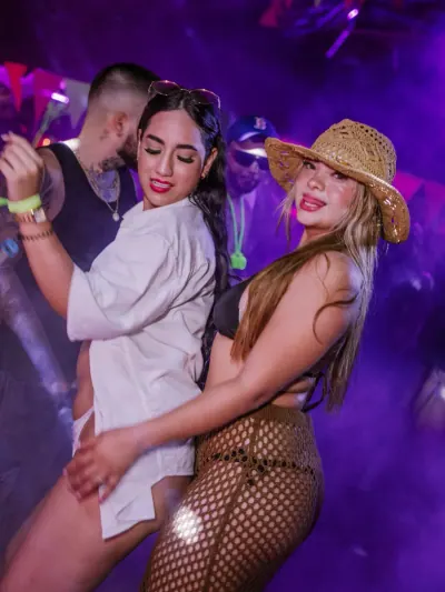 Personas bailando entre luces violetas y humo durante una fiesta nocturna.