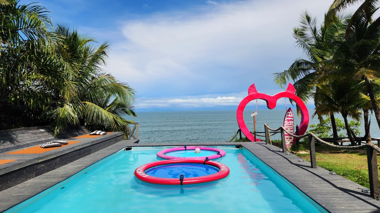 Piscina y columpio rosa con forma de corazón frente al mar.