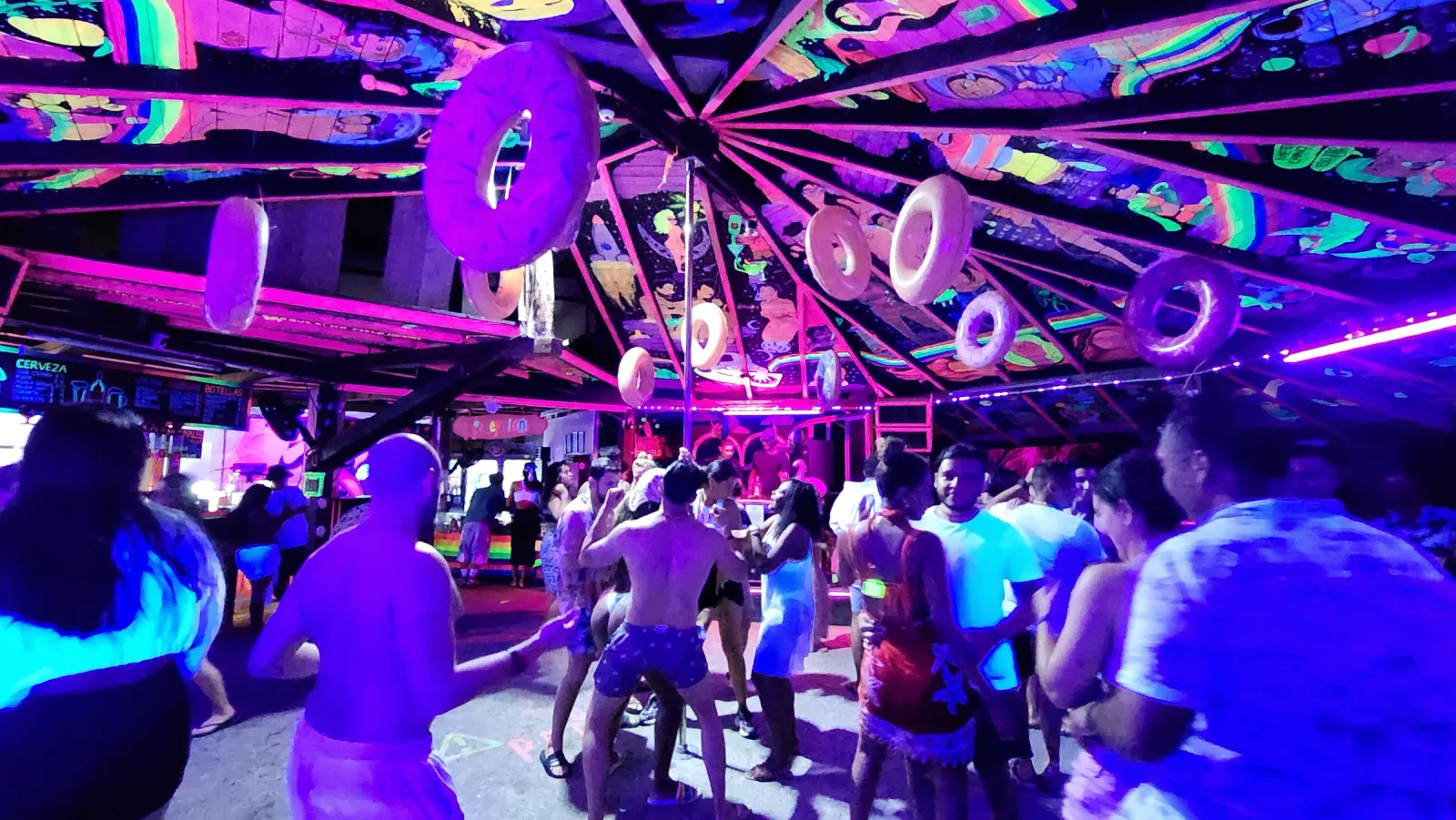 Público bailando bajo un techo con ilustraciones fluorescentes.