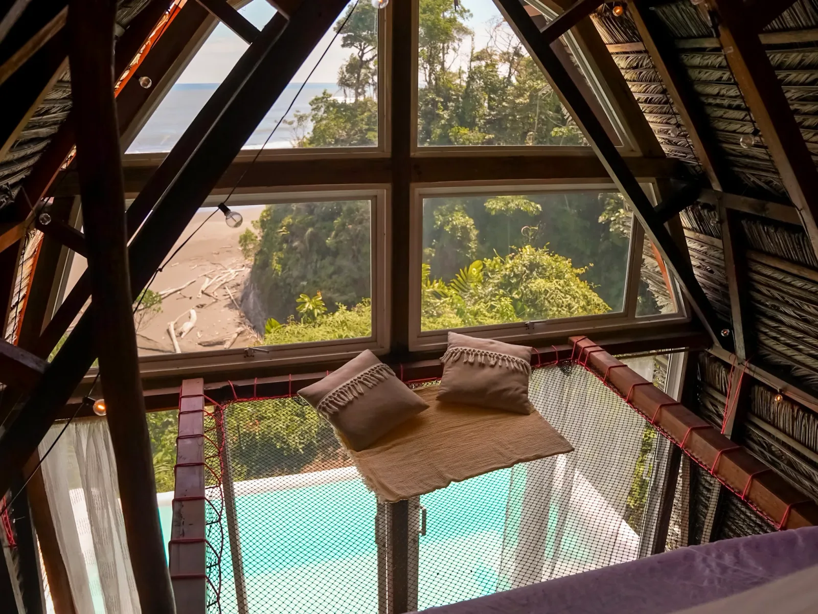Interior de una suite triangular con cama de red, piscina y vista a la costa.