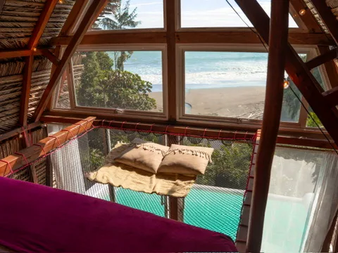 Interior de una suite triangular con cama de red, piscina privada y vista al mar.