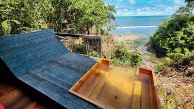 Tina privada de madera en una habitación abierta con vista panorámica a la costa.