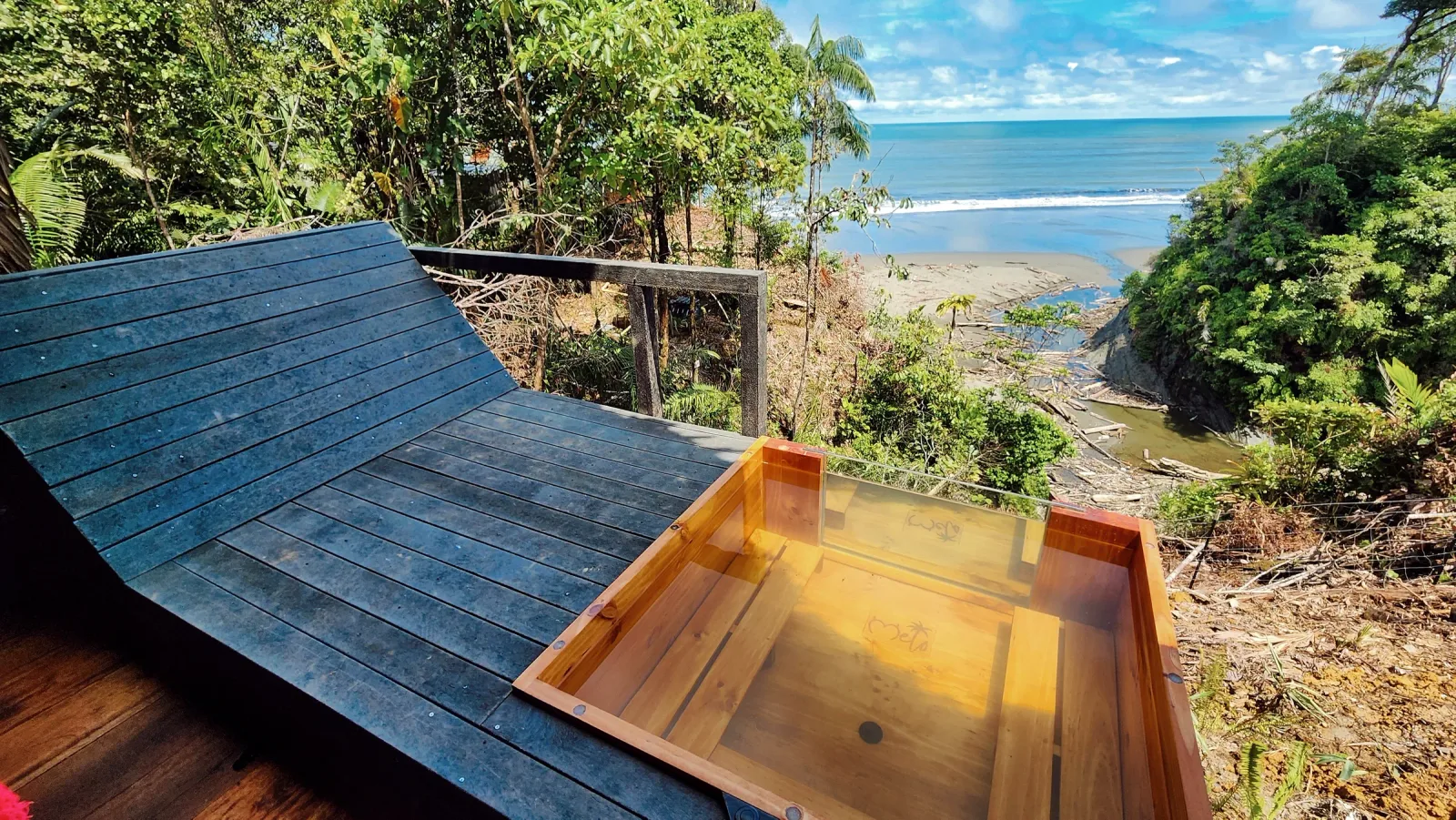 Tina privada de madera en una habitación abierta con vista panorámica a la costa.