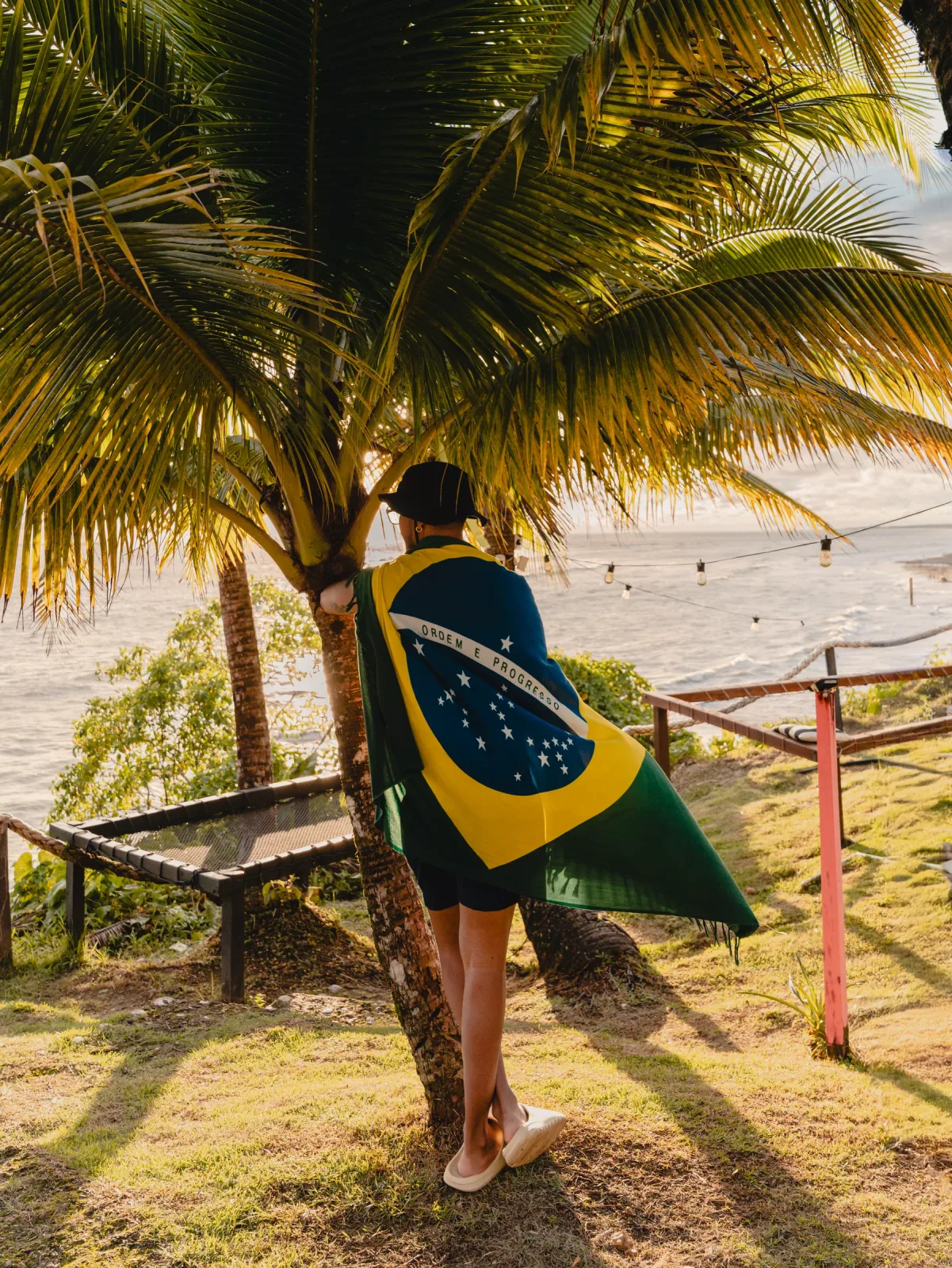 Visitante cubierto con la bandera de Brasil frente al mar y las palmeras.