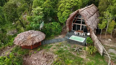 Vista aérea de cabañas tropicales y piscina rodeadas por vegetación.