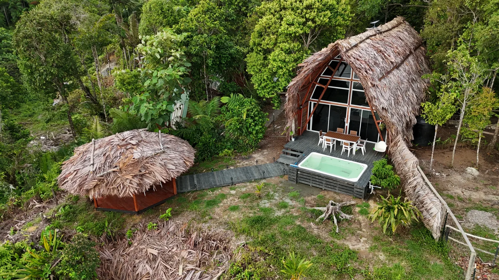 Vista aérea de cabañas tropicales y piscina rodeadas por vegetación.