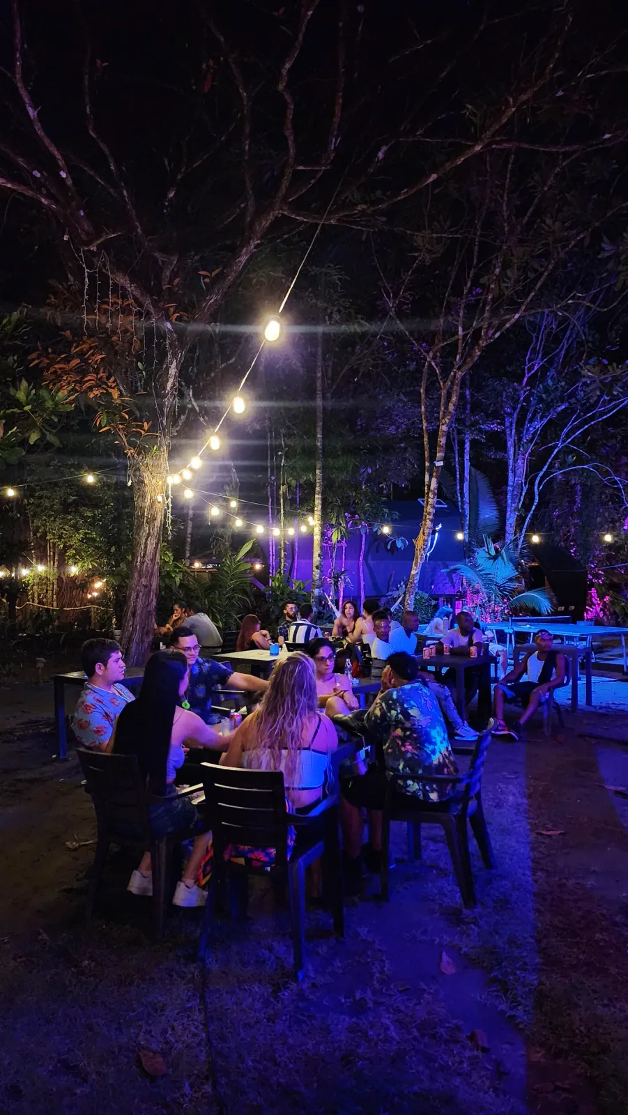 Zona social al aire libre iluminada con luces azules y violetas durante la noche.