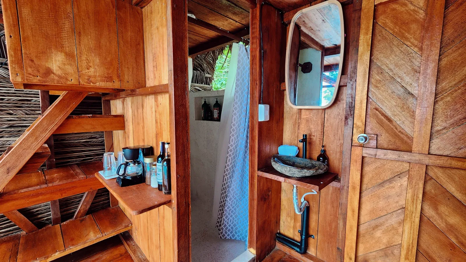 Baño de madera con lavamanos de piedra, ducha y estación de café.