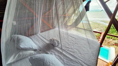 Cama con mosquitero junto a una piscina privada y vista directa al mar.