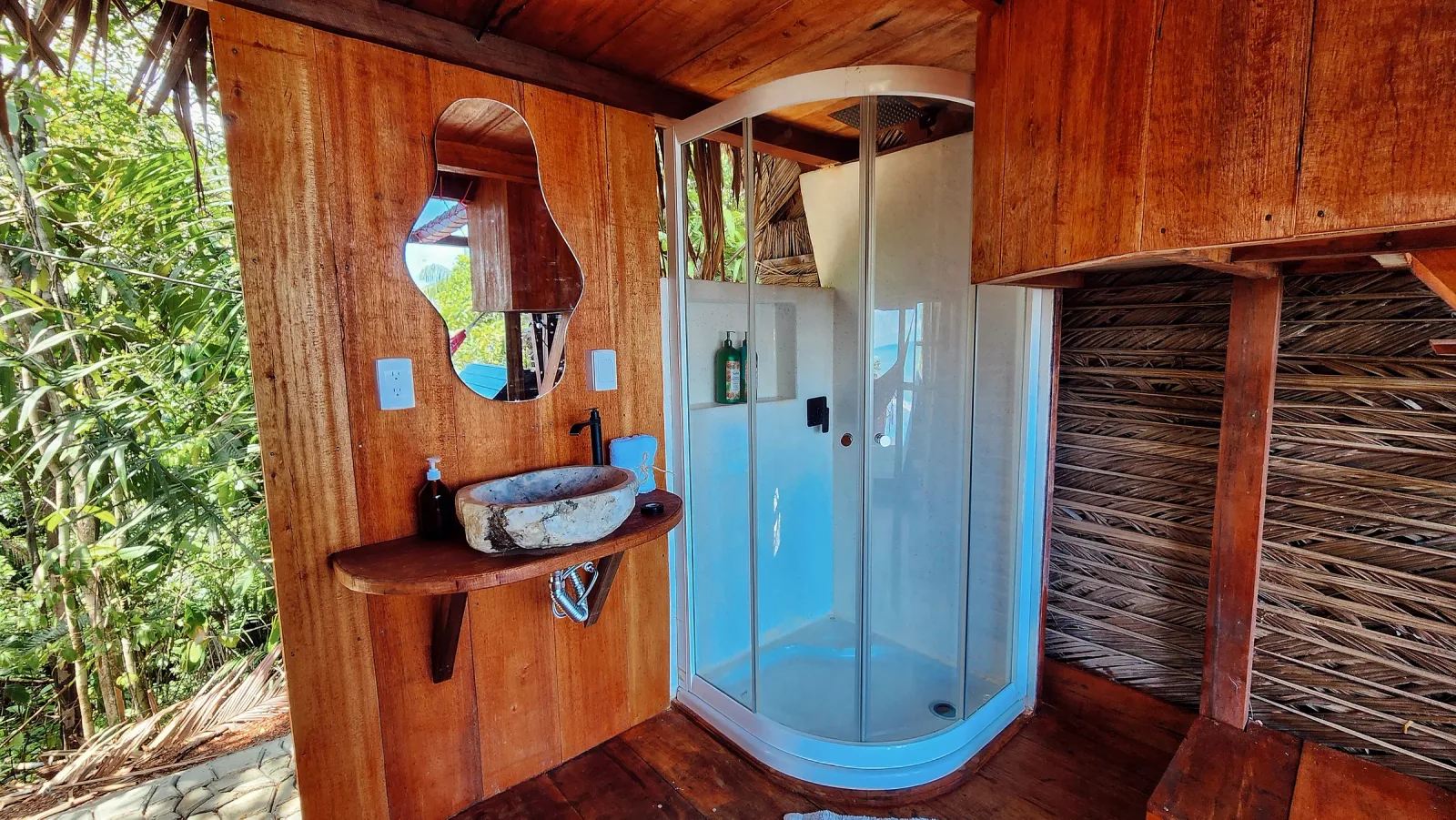 Baño privado con ducha curva, lavamanos de piedra y acabados en madera.