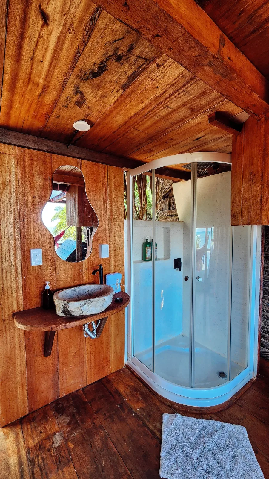Baño privado con ducha curva y lavamanos de piedra en formato vertical.