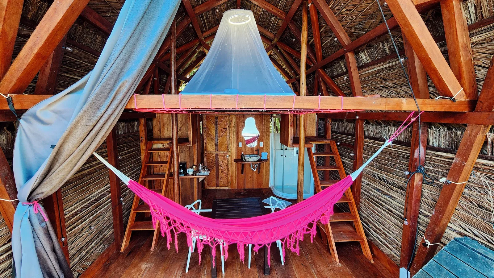 Interior de Metemelo con hamaca rosa, cama elevada y baño privado.