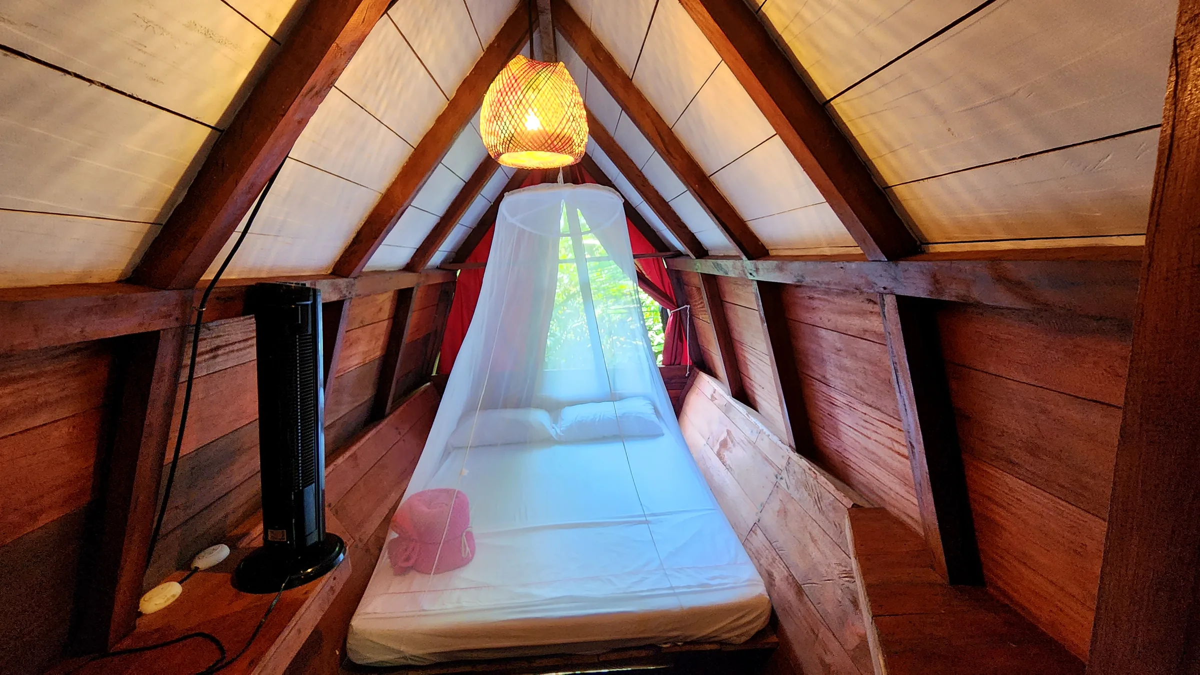Cama de la habitación Mandarina bajo una lámpara de fibras naturales.
