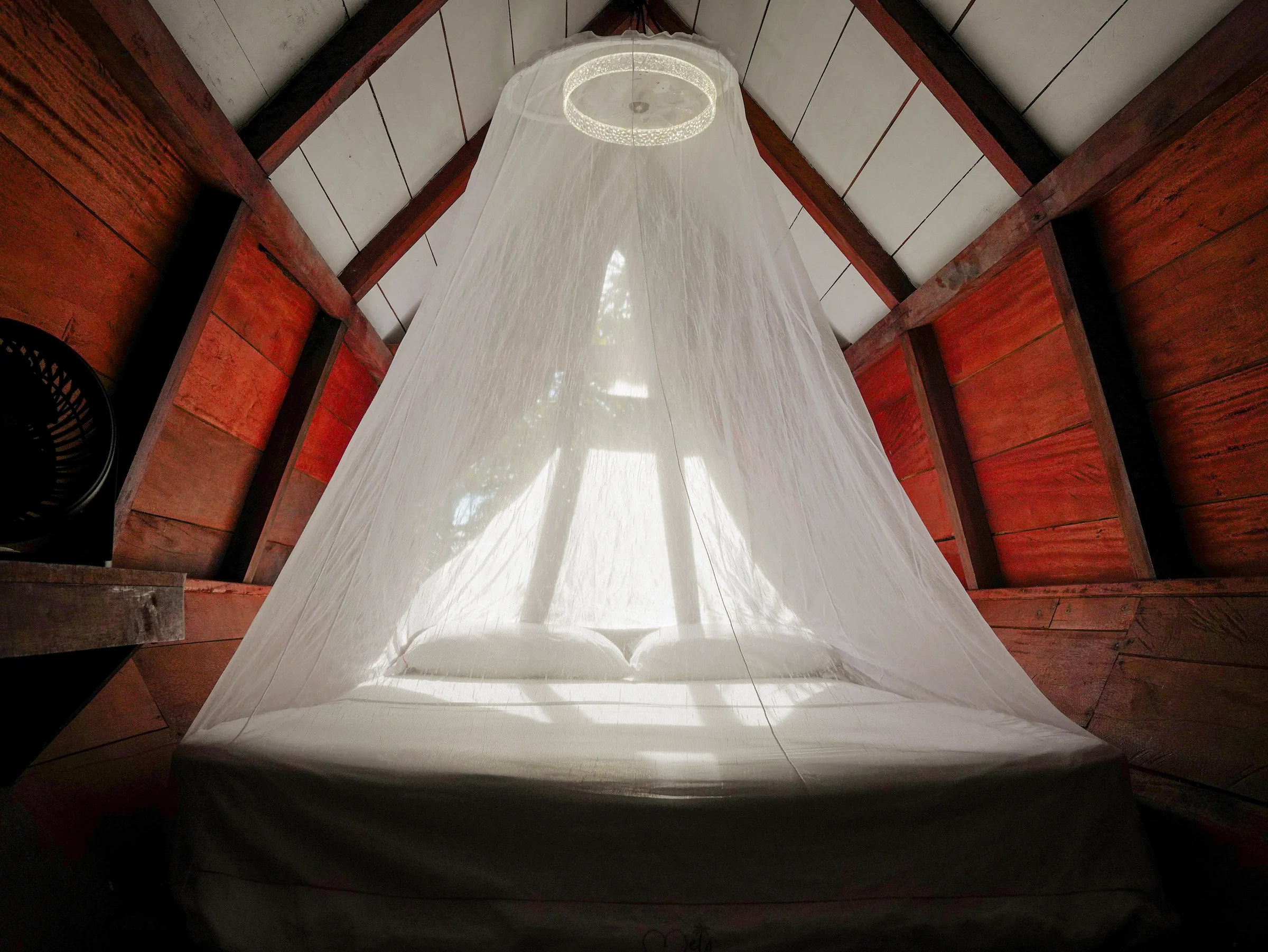 Cama con mosquitero centrada bajo el techo triangular de la habitación Mandarina.