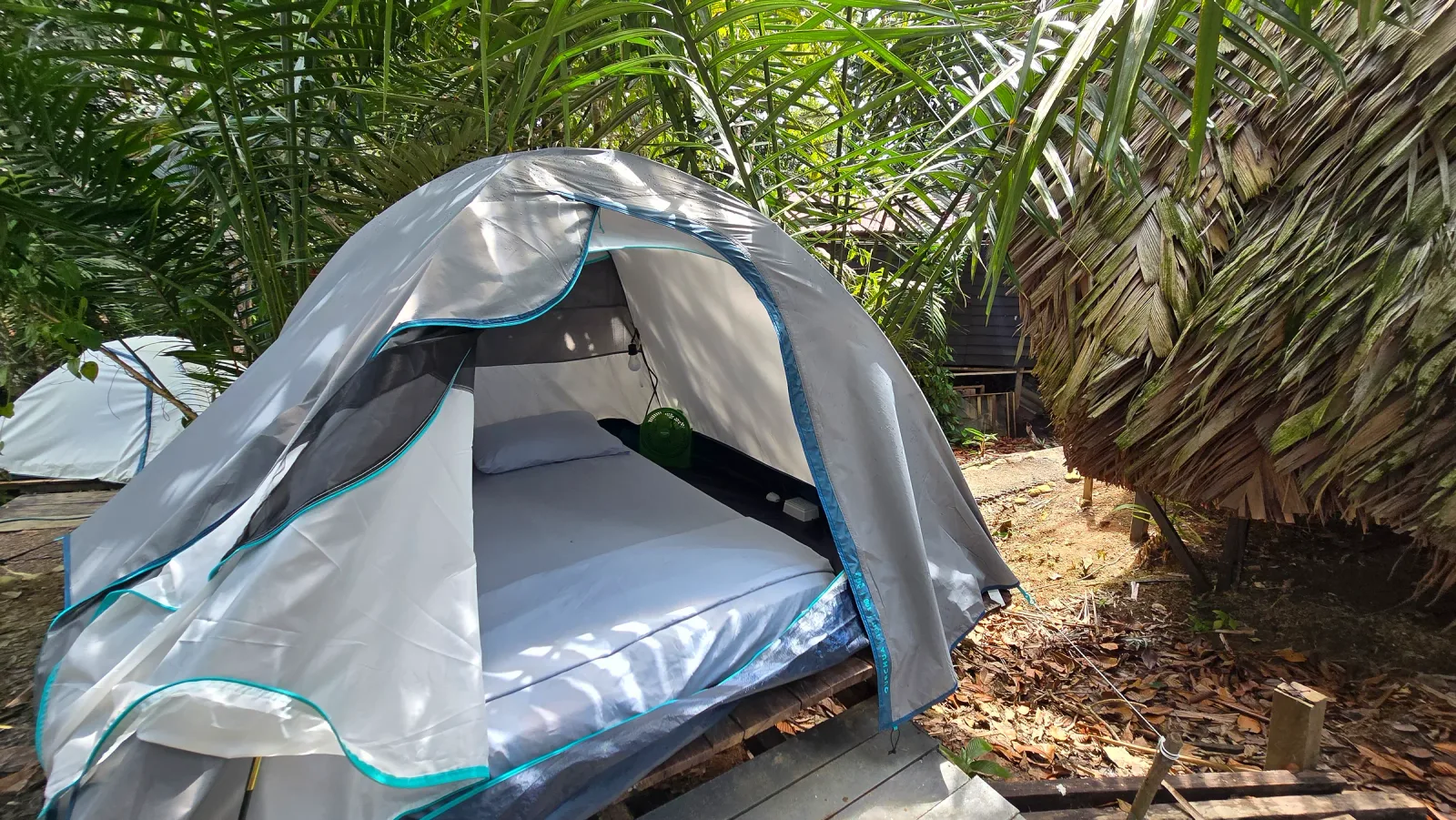 Carpa abierta con cama doble sobre una plataforma entre vegetación tropical.