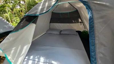 Interior de una carpa con cama doble, ropa blanca y ventilación lateral.