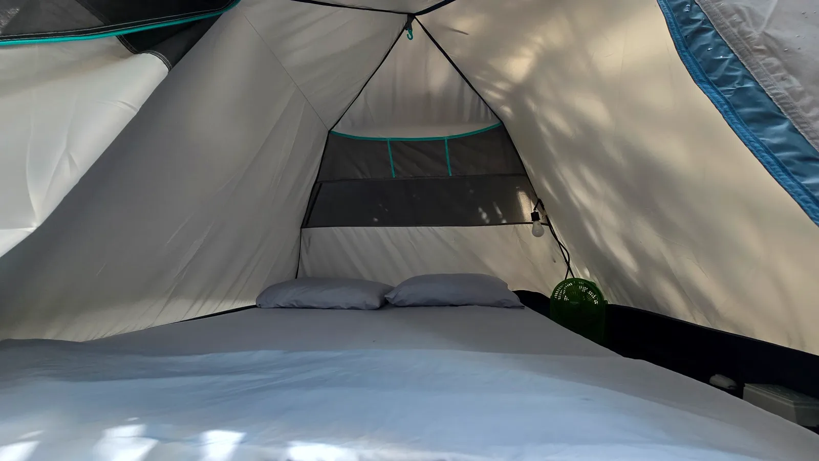 Cama doble preparada dentro de una carpa con paredes claras.